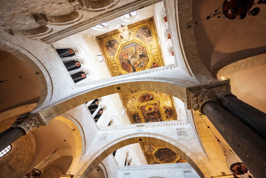 A church ceiling with tall stone arches and golden ceiling frescoes in between.
