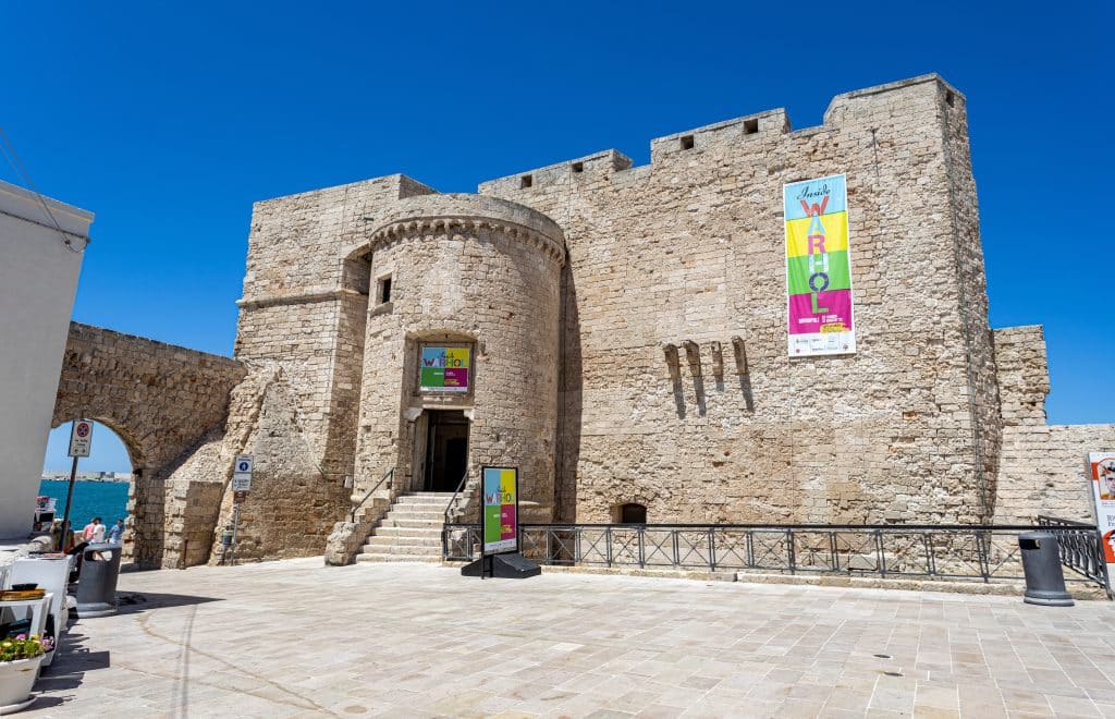 A square stone castle perched on the edge of the sea in Monopoli, Italy.