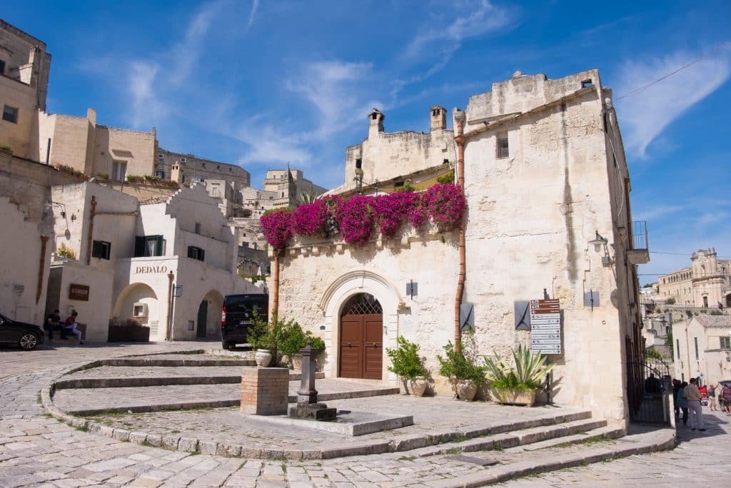 A ramp leading around a stone church topped with purple flowers in Matera.