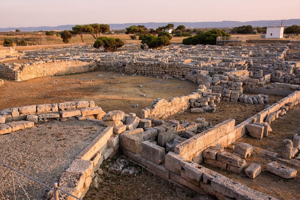 Stones laid out in circles in archaeological ruins under purple sunset light.