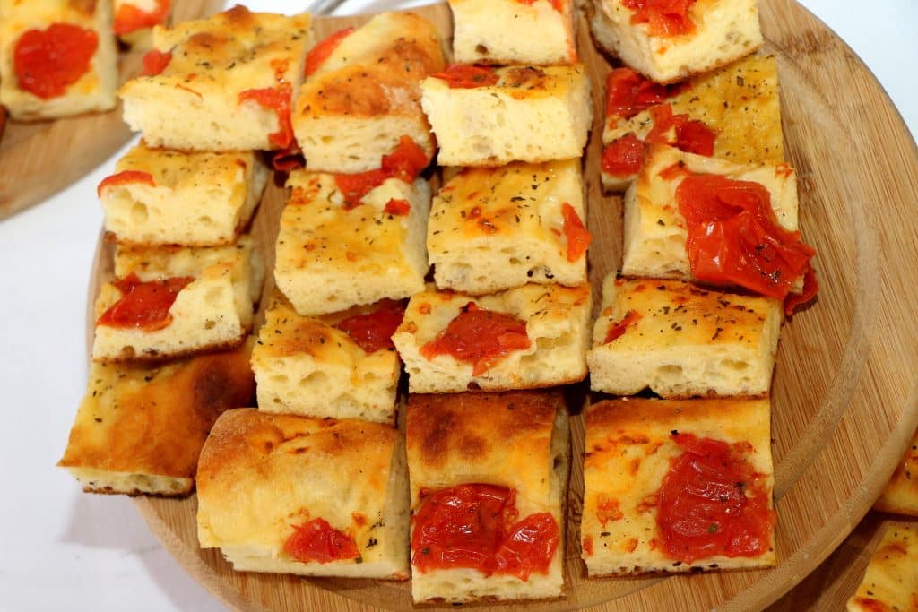 A plate with several bite-sized pieces of focaccia topped with tomatoes.