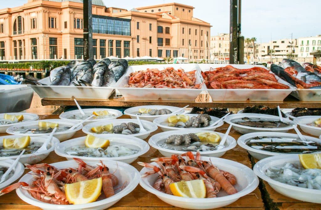 A seafood market in Bari, Italy, with paper plates covered with shrimp and lemon slices.