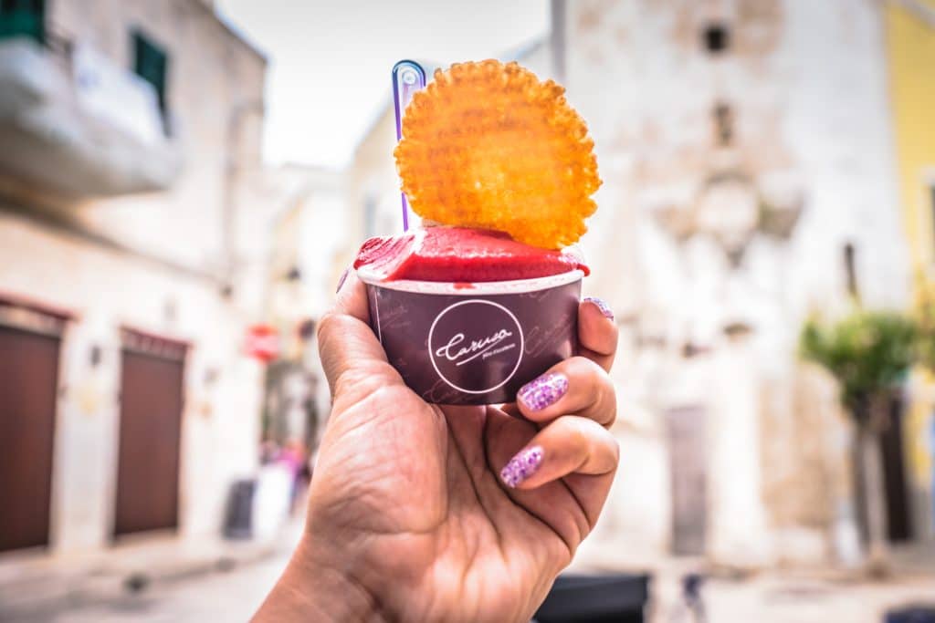 A hand holding a cup of Gelato in the middle of an Italian old town.