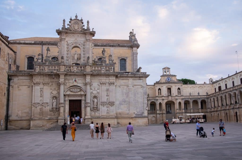 A big church set on a piazza in Italy, with a crowd of people with kids walking around in front of it.