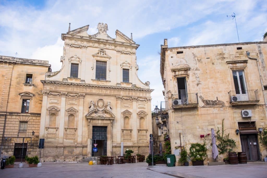 A Baroque church covered with ornate stone details on a piazza in Lecce, Italy.