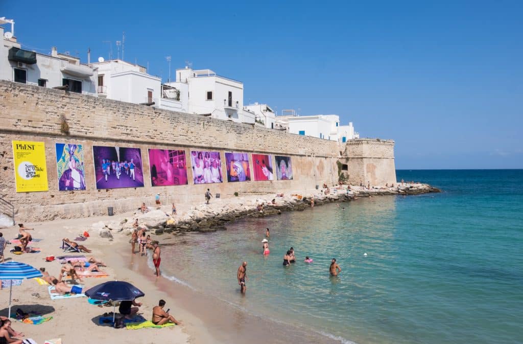 A small beach leading to turquoise water next to a stone city wall in Monopoli.