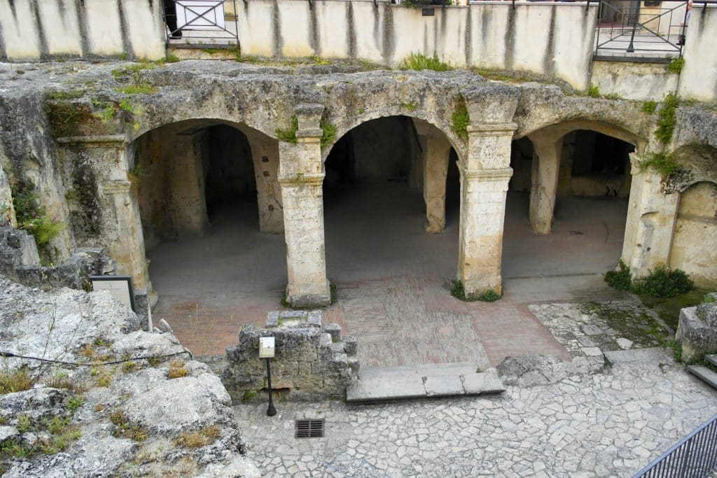 The Palombaro Lungo, a gateway to an underground area in Matera with arched columns covered with overgrown vegetation.