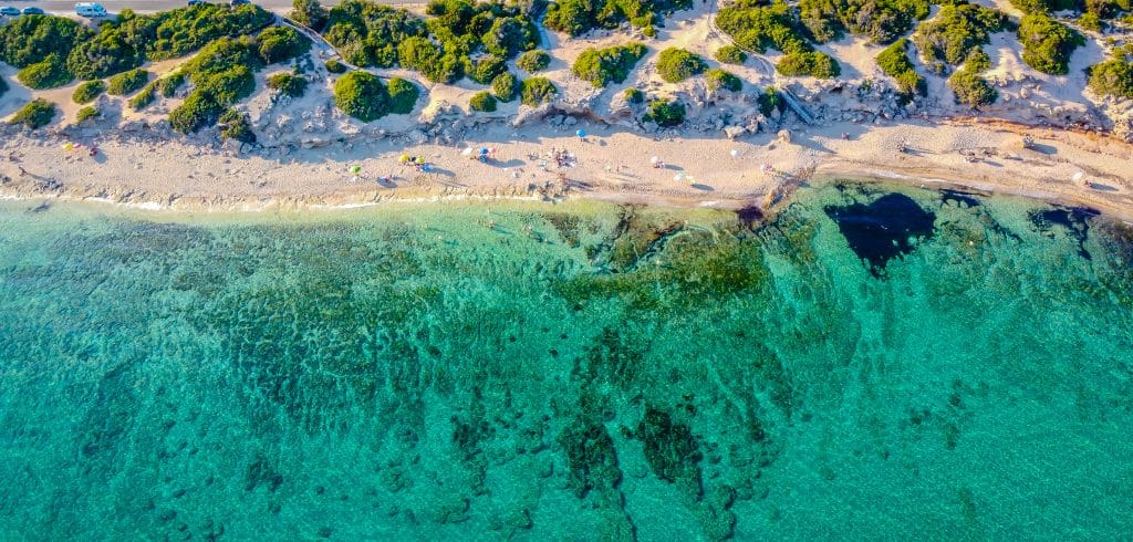 Vue aérienne de la magnifique Punta Prosciutto en Italie, avec des personnes se prélassant sur du sable doux devant une eau claire d'un turquoise éclatant.