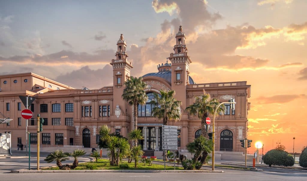 A theater in Bari Italy set against the sunset. The theater is sand-colored and has two spindly towers.