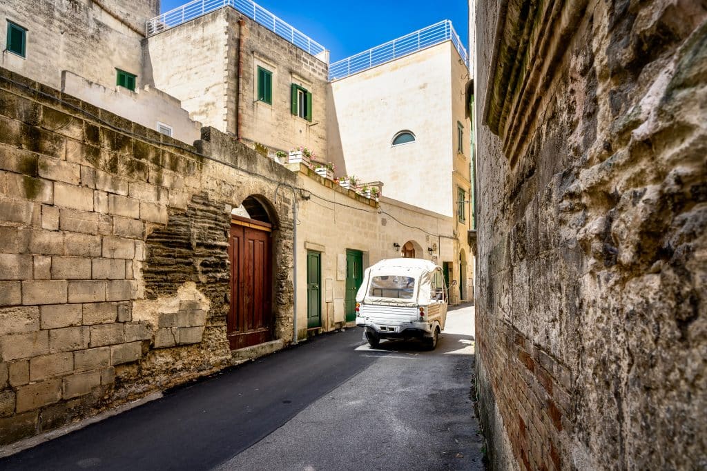 Un petit tuk tuk blanc circulant dans les rues en pierre de Matera.