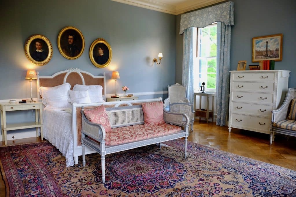 Edith Wharton's ornate bedroom at The Mount, decorated in pale pink and blue with framed portraits on the walls.