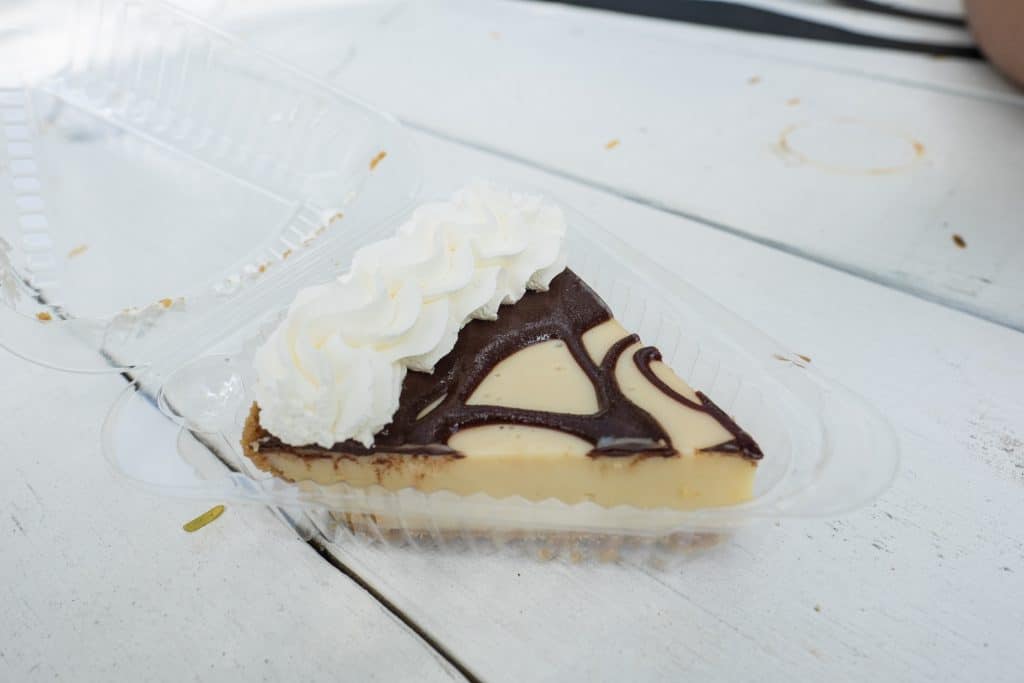 A slice of chocolate syrup-topped key lime pie in a plastic container.