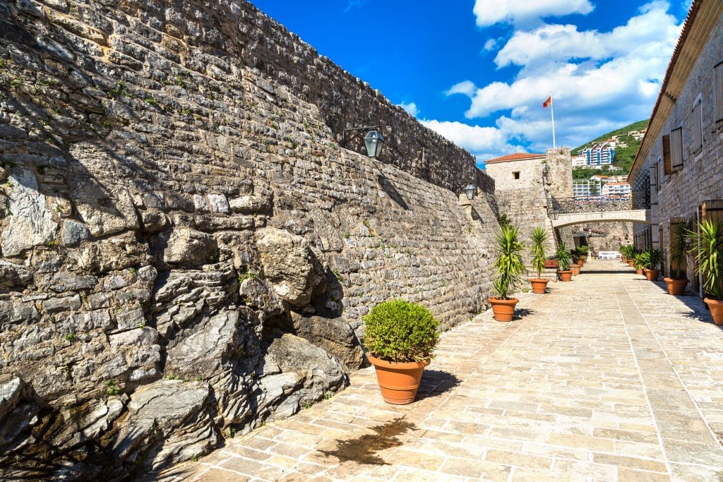 A pathway along a stone wall in a fortress underneath a bright blue sky.
