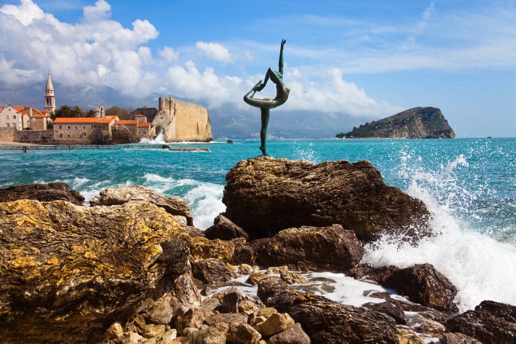 A statue of a ballerina posed on a rock in Montenegro, with waves crashing around it.