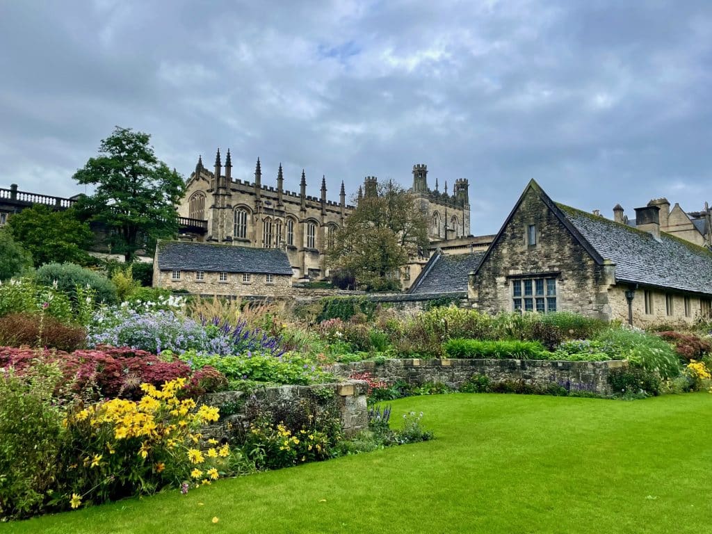A gothic church and bright flower garden underneath a cloudy sky.