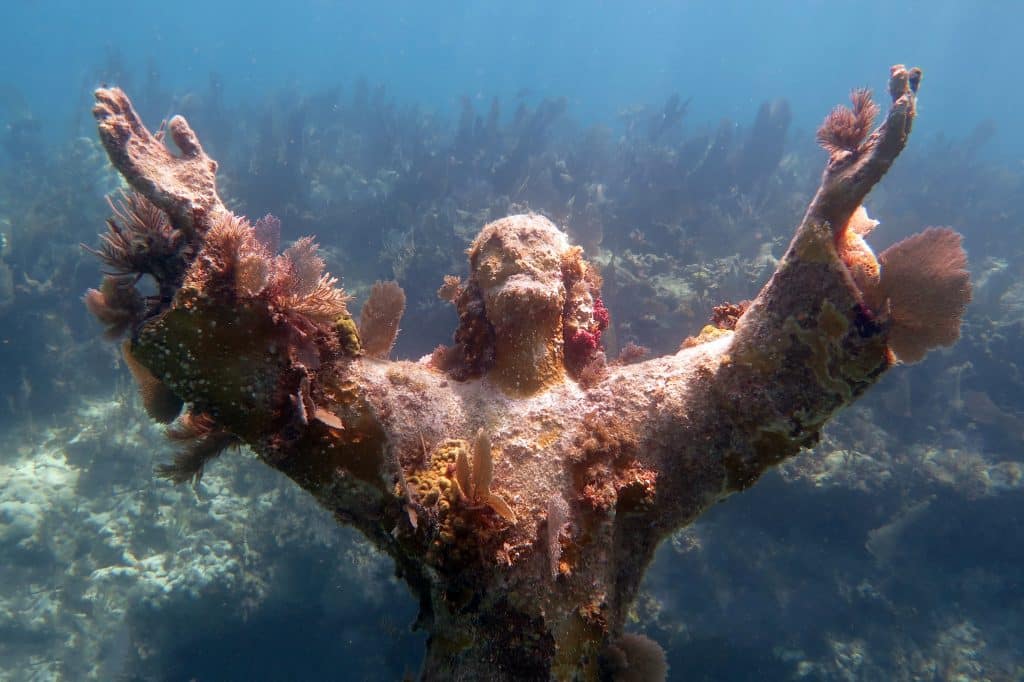 An underwater statue of Jesus reaching his arms up to the surface.