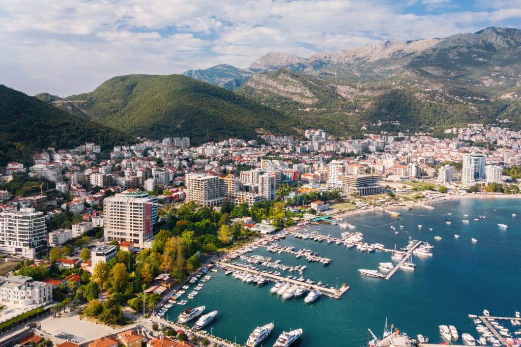 An aerial view of Budva Montenegro: a beach town with green mountains rising in the background, and lots of high-rise buildings close to the beach.