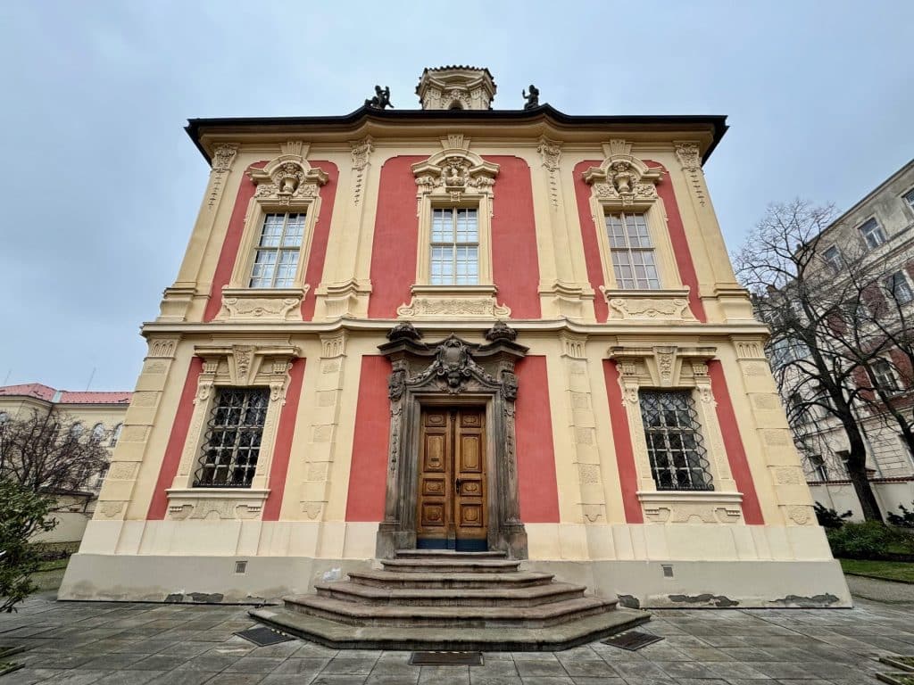 A Baroque building in Prague with pink and yellow walls and a big wooden door.