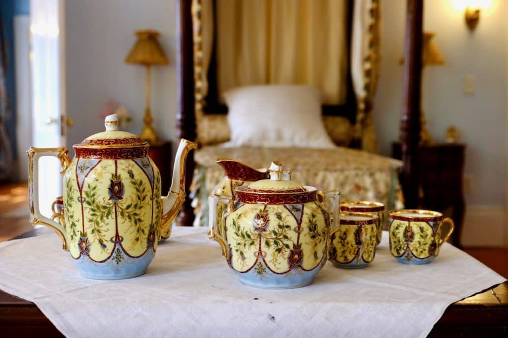 A Victorian-era tea set made of fine china in pale yellow, set in a bedroom.