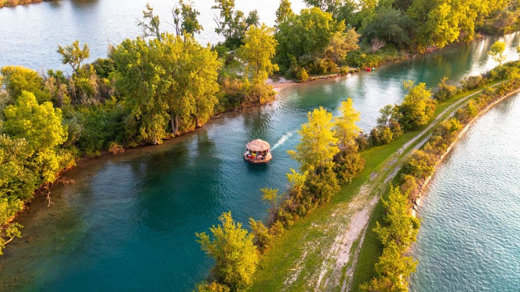 A round raft with a small tiki hut on it floating down a river surrounded by mangroves.