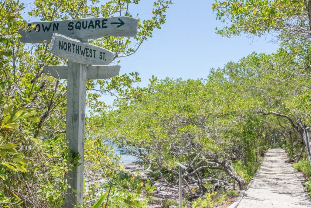 A boardwalk leading through the mangroves on a small island. A weathered wooden sign has directions to the town square and Northwest st.
