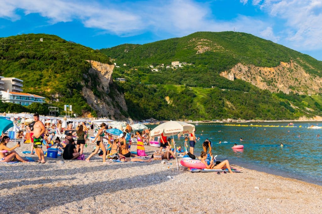 People lounging on a rocky beach in Montenegro, green cliffs in the background.