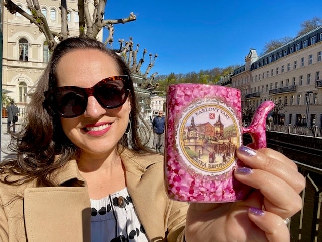 Kate taking a smiling selfie and holding up a small pink water jug with a scene from Karlovy Vary painted on it.