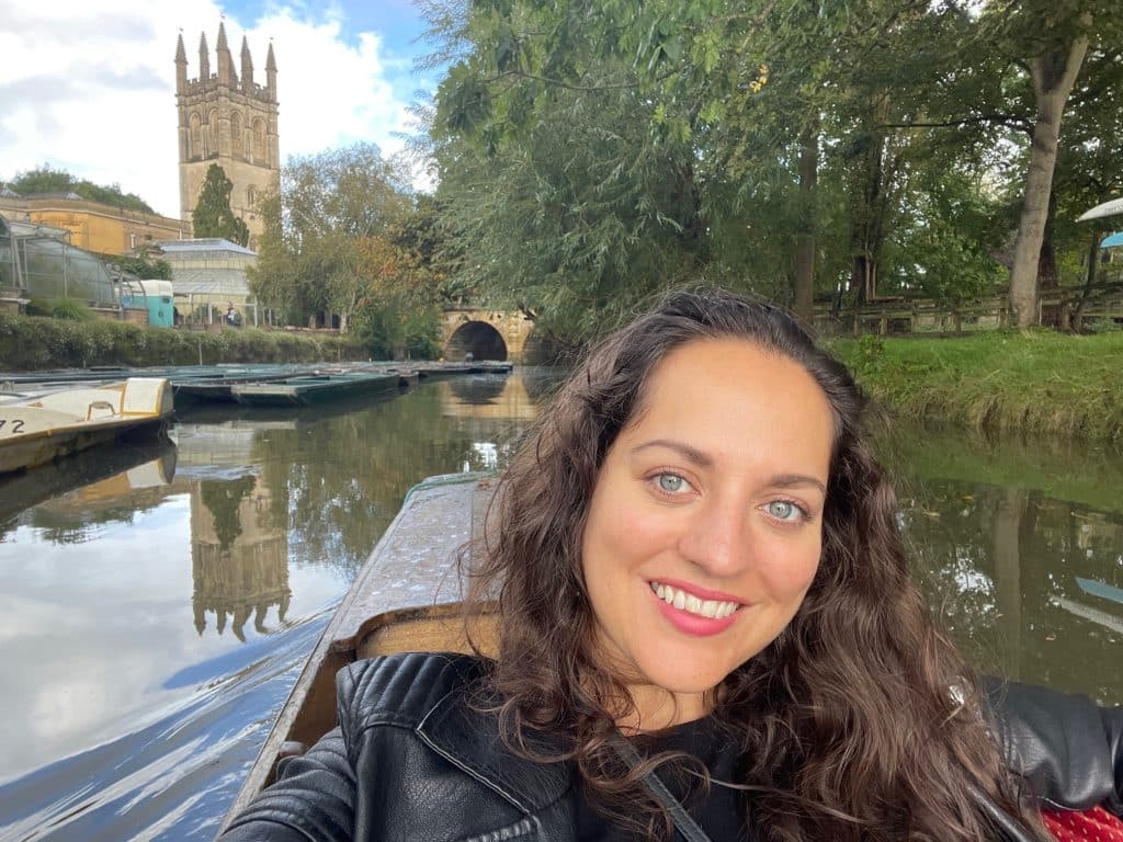 Kate lying back on a river boat in Oxford, with a church tower behind her reflecting in the water.
