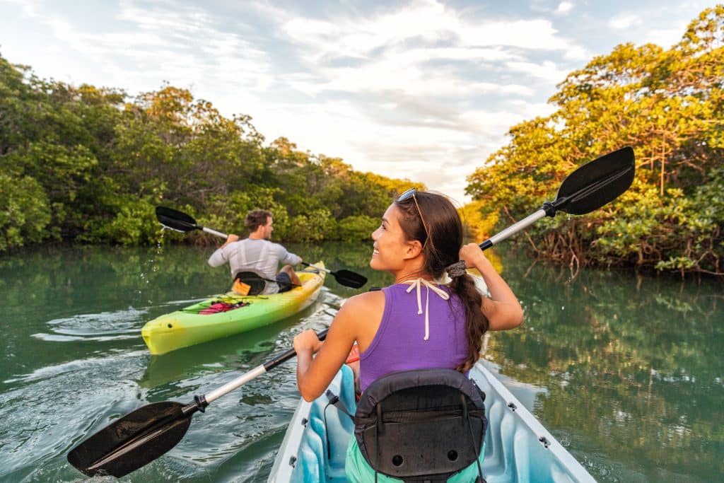 A man and woman kayaking in their own kayaks, along a river edged with mangroves.
