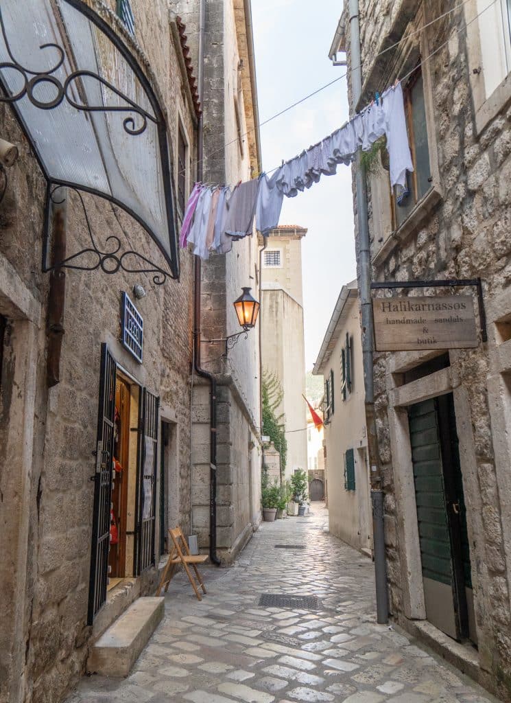 A narrow alleyway in the old town of Kotor, buildings and ground made of stone, with a line of white laundry hanging overhead.