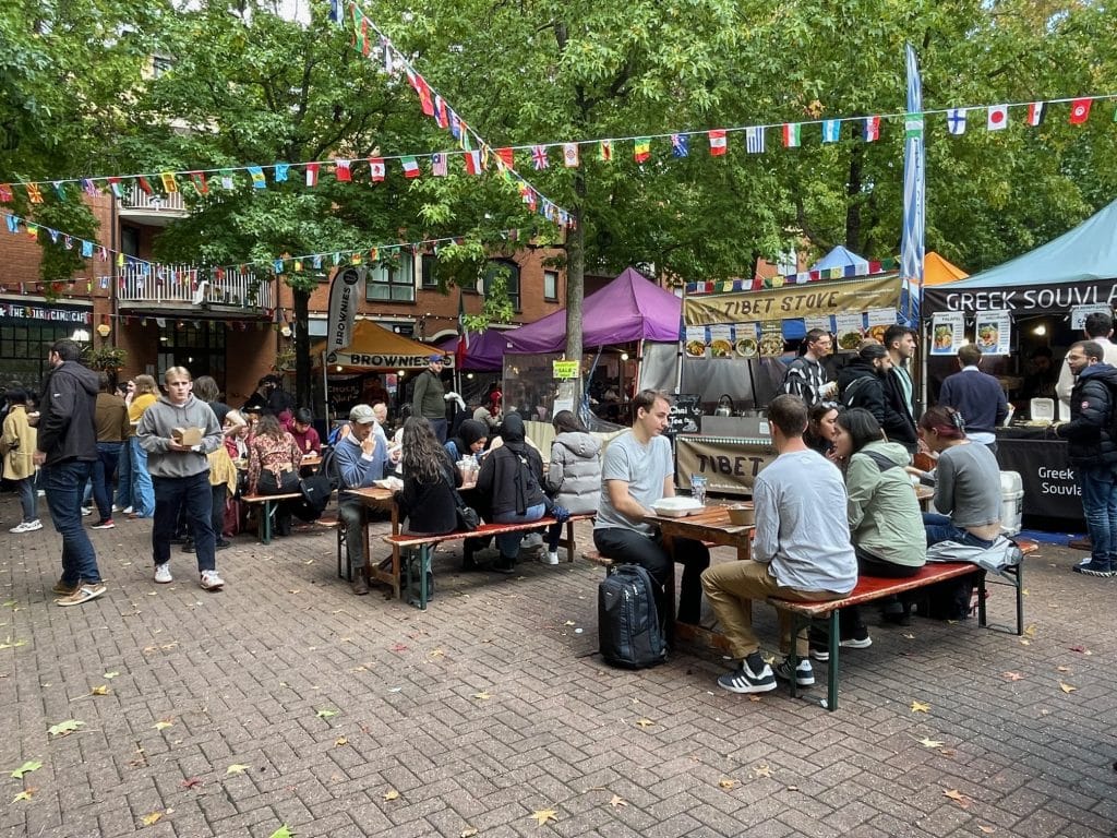Young people eating an an outdoor food market with lots of food stalls.