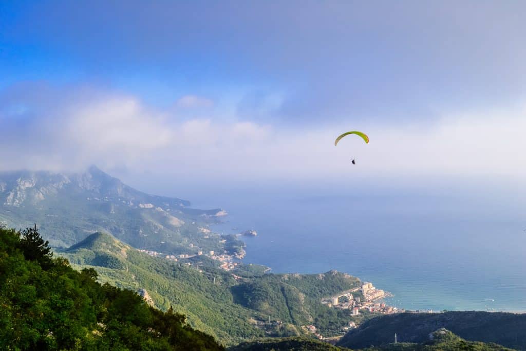 A paraglider high in the air above the rocky, dramatic coastline of Montenegro.