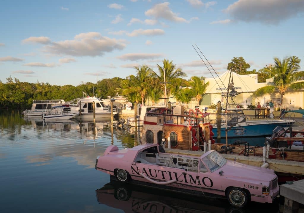 Une Cadillac rose transformée en bateau, assise sur un quai dans les Keys de Floride, avec des palmiers en arrière-plan.