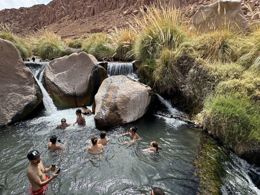 People luxuriating in pools beneath waterfalls in the middle of a canyon in the desert.