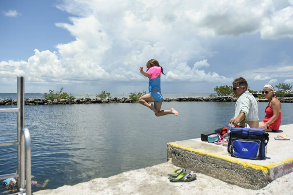 A young girl in water wings jumping into a lake as her parents look on.