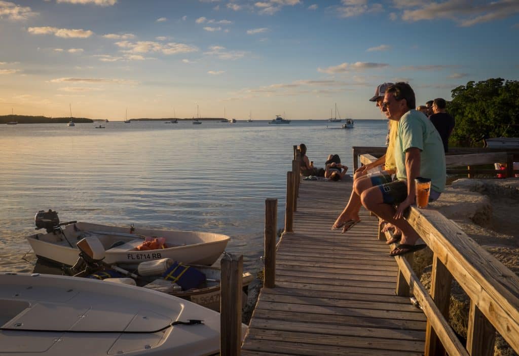 People sitting on a wooden dock in the Florida Keys, enjoying the view just before sunset.
