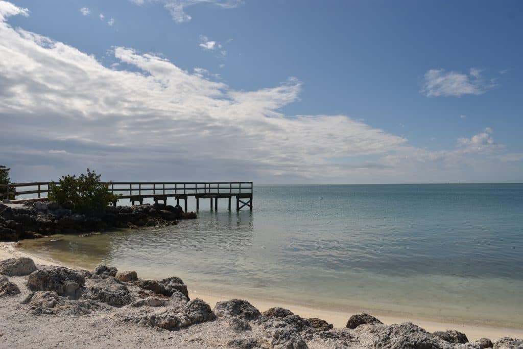 A calm sandy beach with a wooden pier jutting out into the water.