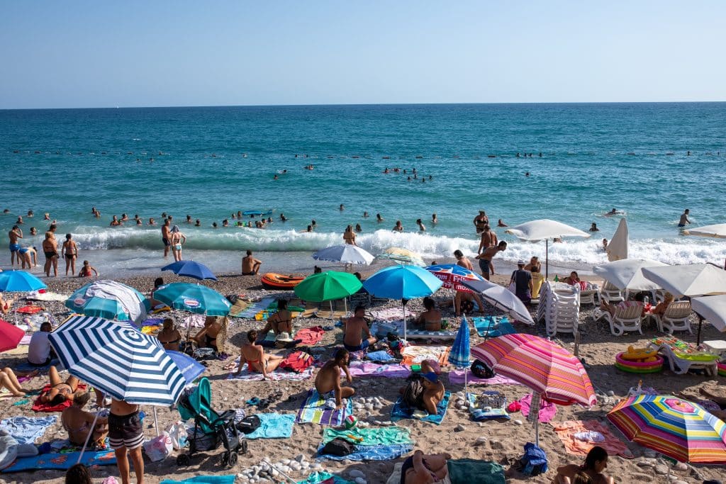 A pebbly beach crowded with lots of people and umbrellas.