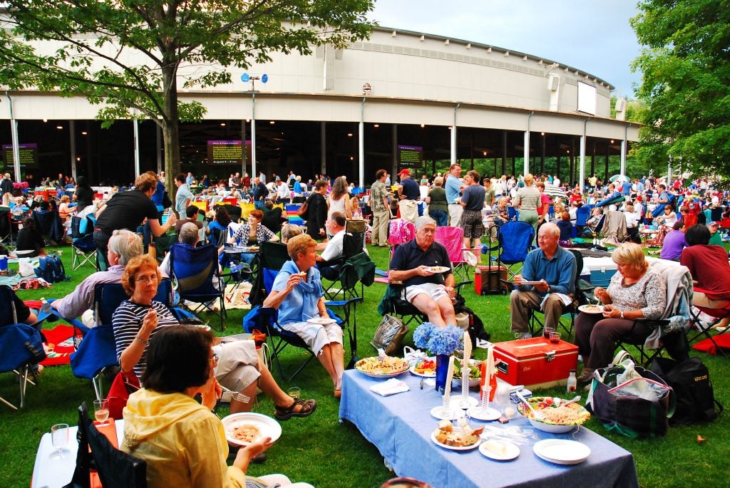 A big crowd of people picnicking around the Tanglewood theater in Lenox Mass.