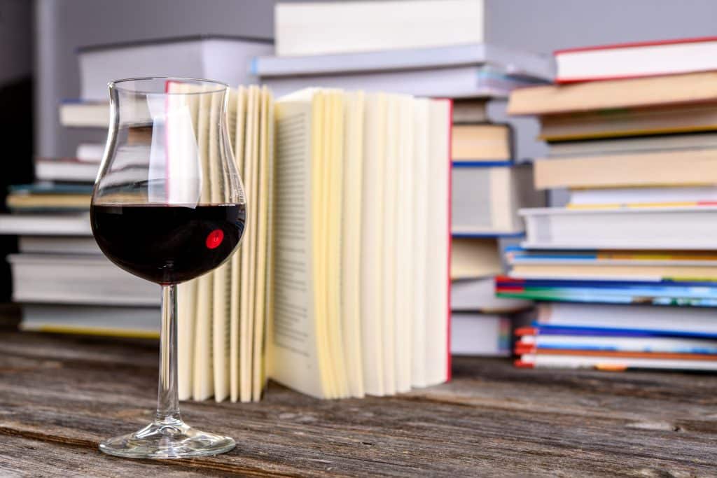 A red wine glass in front of a pile of books.