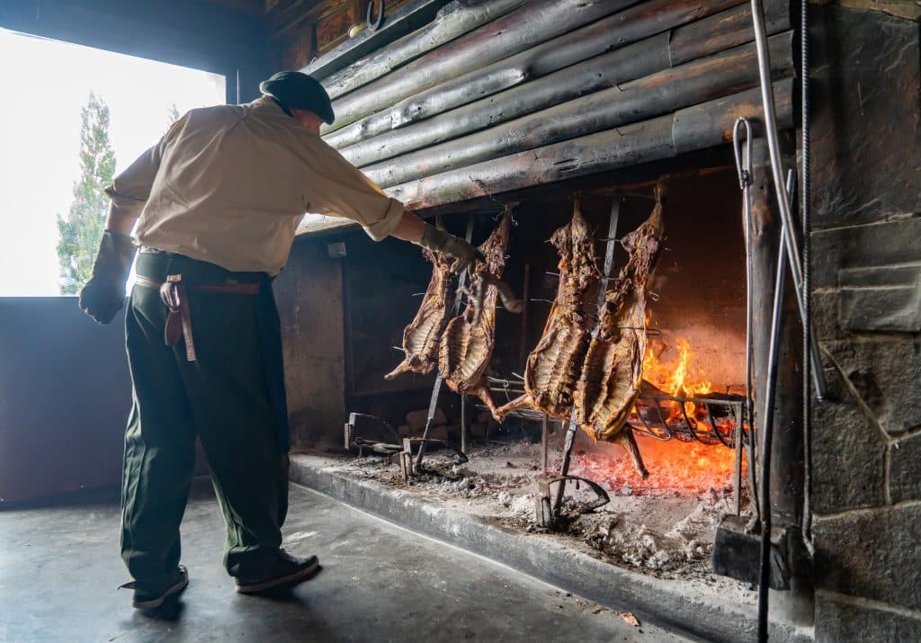 A man checking on sides of lamb roasting over a fire.