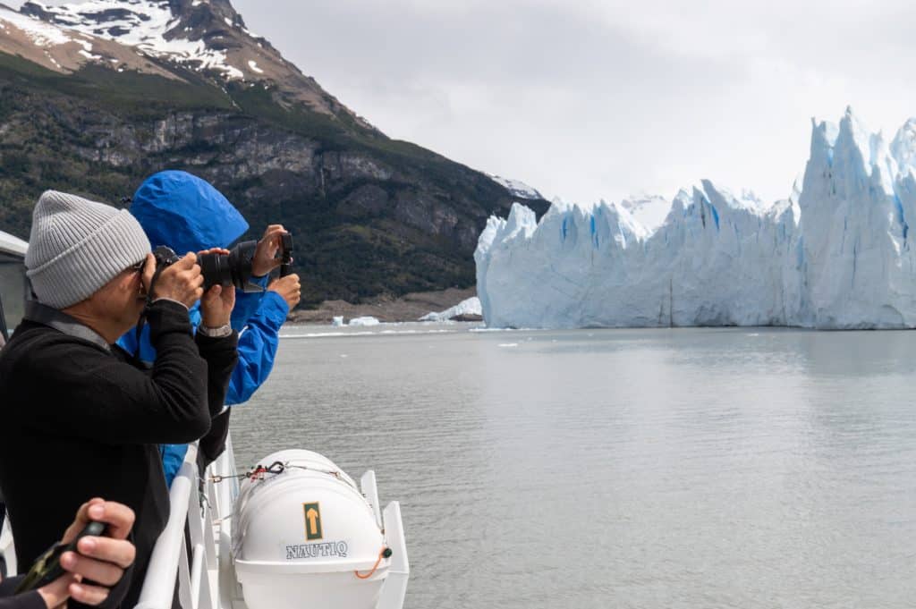Two men on a glacier cruise photographing Perito Moreno Glacier in the distance.