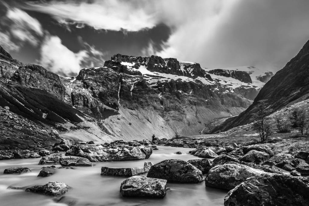 A black and white shot of a big white glacier on top of a jagged mountain.