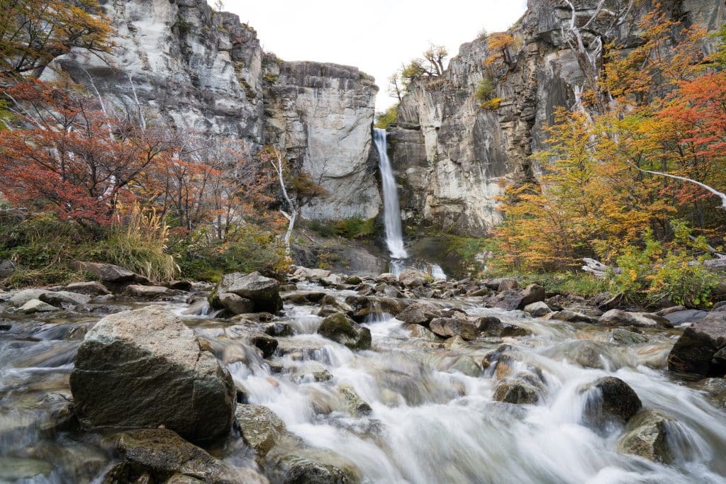 A waterfall falling between two rock falls, surrounded by red and orange fall foliage.