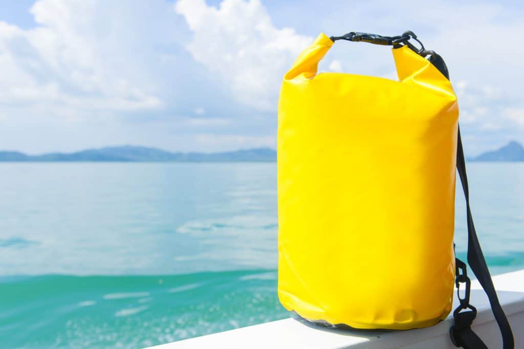 A bright yellow dry bag perched on the edge of a boat, overlooking clear turquoise water.