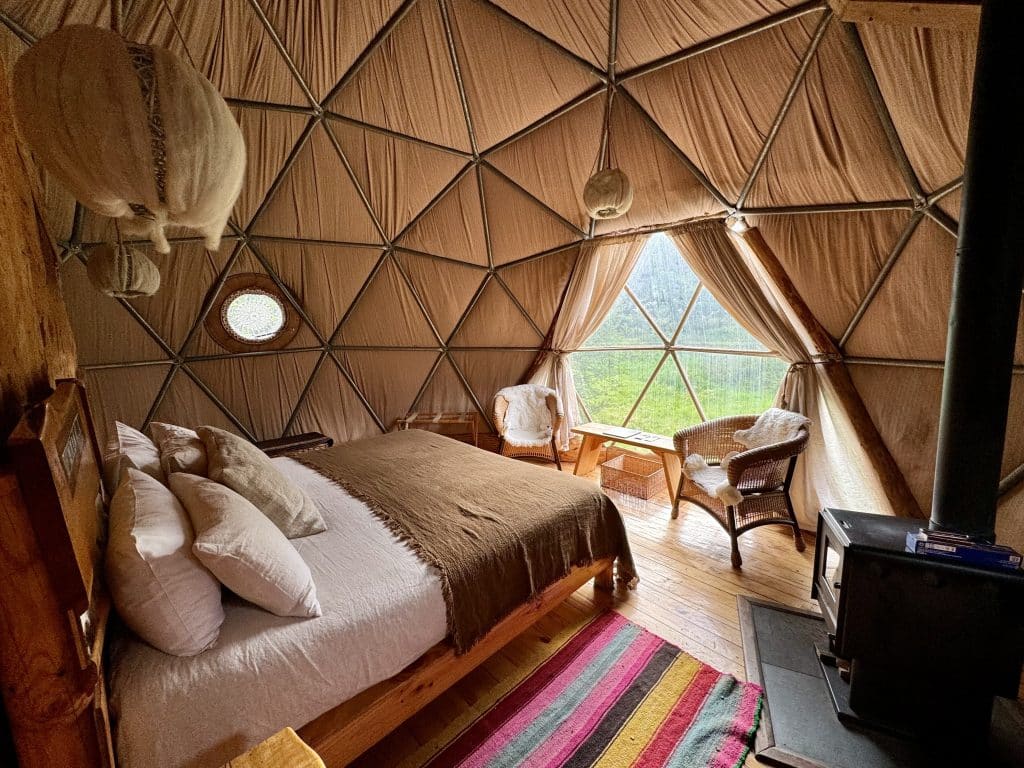 A dome hotel room, with a big king-sized bed covered with blankets, some chairs topped with fur blankets, and a wood stove.