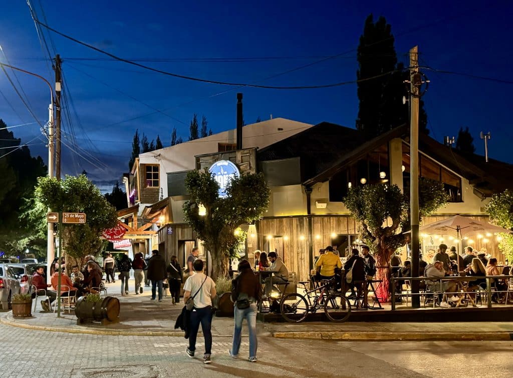 People walking down a busy street in El Calafate at night, the sky deep blue and string lights illuminating everything.