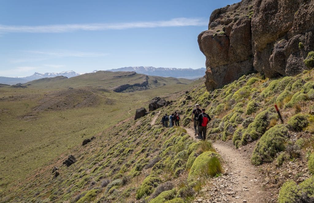 People hiking along a well-worn trail in a hilly area of Patagonia with no trees.