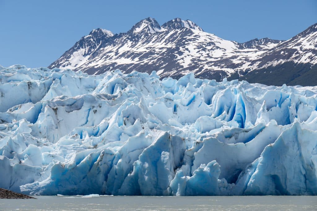 A huge blue and white iceberg, looking like frosting with lots of peaks and nooks and crannies, a big purple-gray mountain behind it.