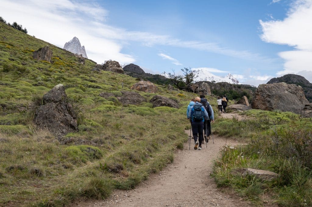 A group of people hiking uphill, gray mountain peaks in the distance.